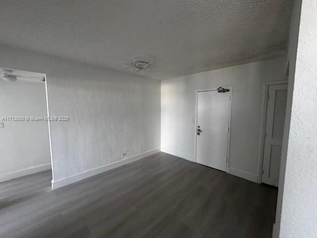 spare room with baseboards, a textured ceiling, and dark wood-type flooring
