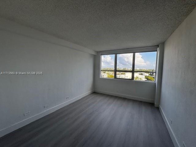 empty room with a textured ceiling, wood finished floors, and baseboards
