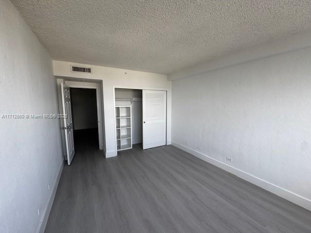 unfurnished bedroom with dark wood-style flooring, visible vents, baseboards, and a textured ceiling