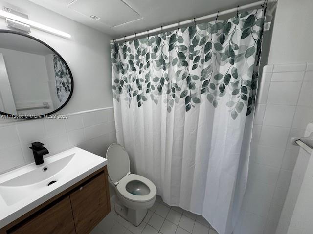 bathroom featuring tile patterned flooring, tile walls, a shower with shower curtain, toilet, and vanity