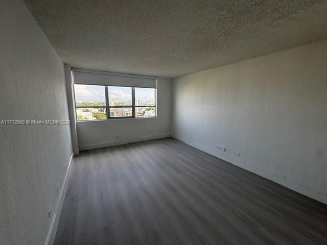 empty room featuring a textured ceiling, wood finished floors, and baseboards