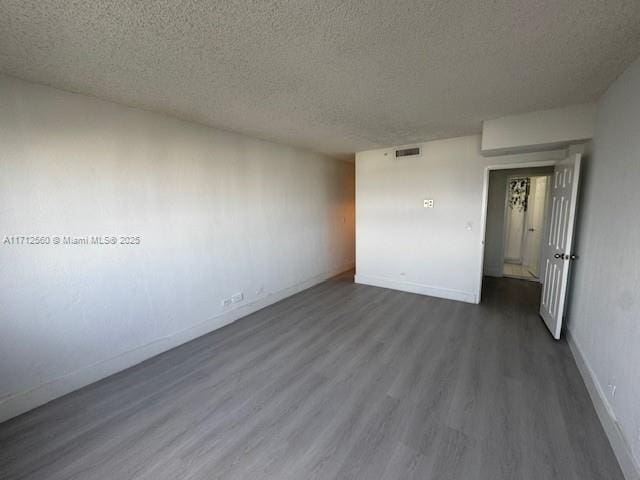 spare room with a textured ceiling, visible vents, dark wood-style flooring, and baseboards