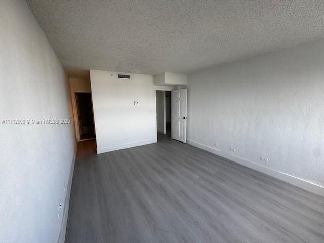 empty room with a textured ceiling, dark wood-style flooring, visible vents, and baseboards
