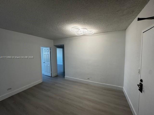 empty room featuring baseboards, wood finished floors, and a textured ceiling