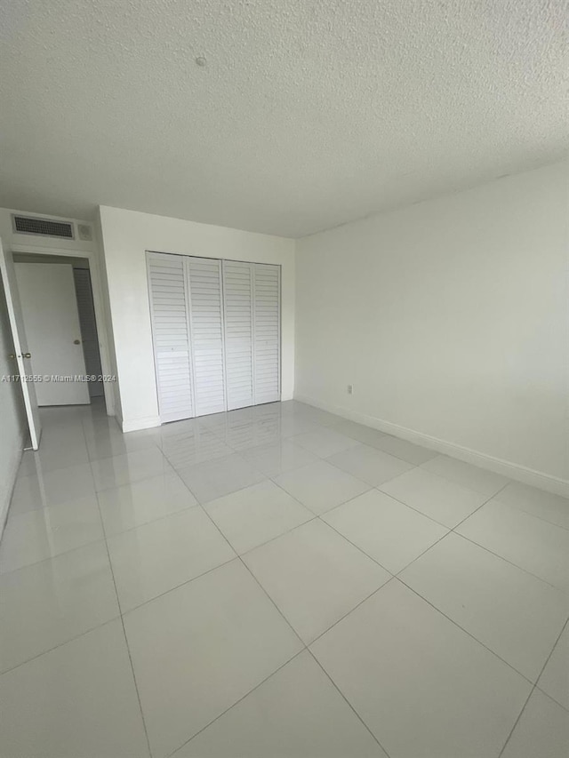 unfurnished bedroom featuring a textured ceiling, a closet, and light tile patterned flooring