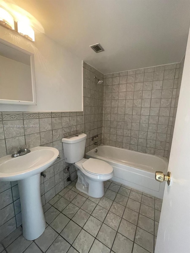 bathroom with tile patterned floors, tiled shower / bath combo, tile walls, and toilet