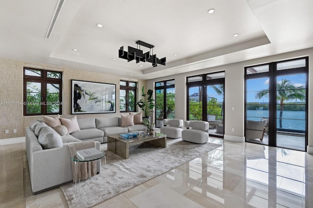 living room featuring french doors, a water view, and a tray ceiling