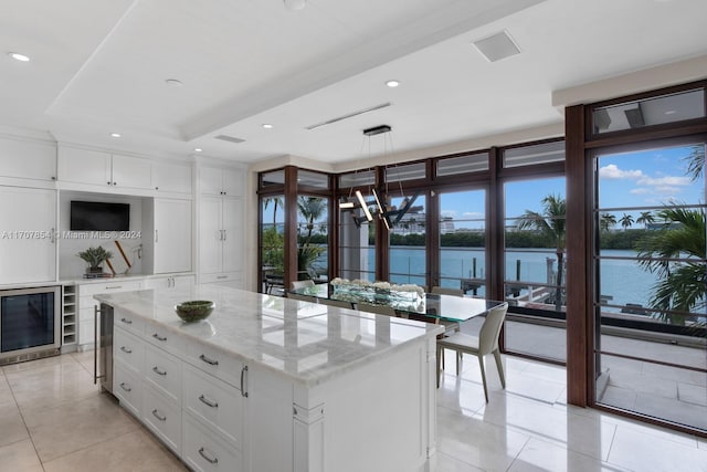 kitchen with beverage cooler, a water view, white cabinetry, a kitchen island, and hanging light fixtures