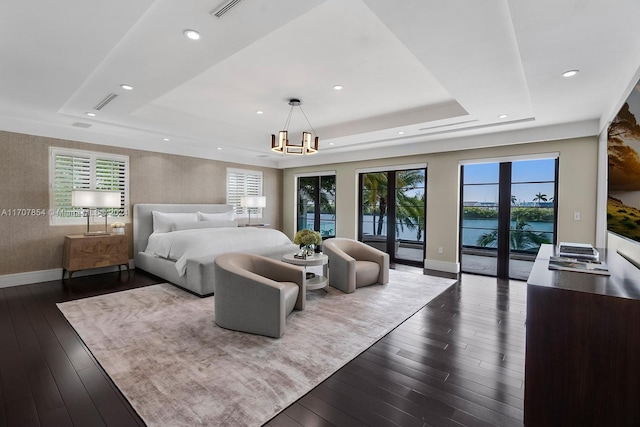 bedroom with a tray ceiling, dark hardwood / wood-style flooring, a chandelier, and access to outside