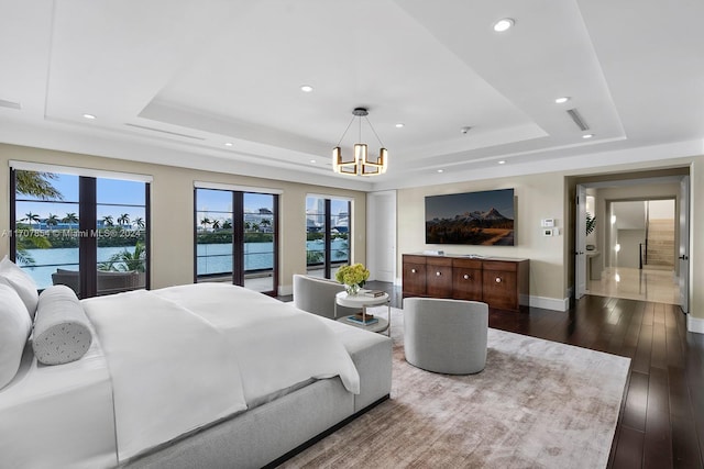 bedroom featuring dark wood-type flooring, a water view, a tray ceiling, and a notable chandelier