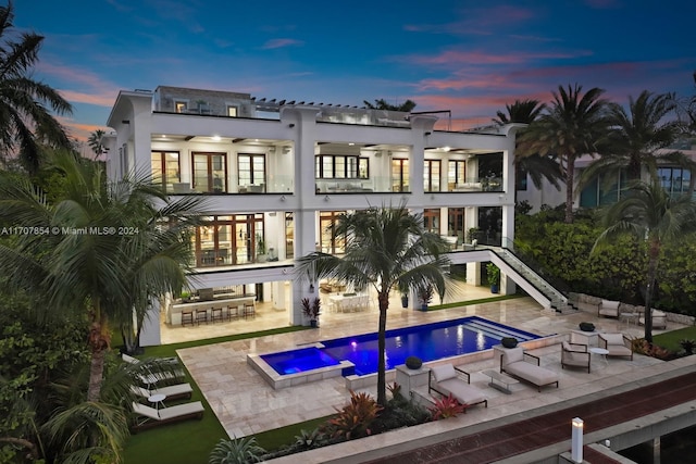 back house at dusk with ceiling fan, a balcony, a patio area, a swimming pool with hot tub, and a bar