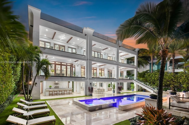 back house at dusk featuring a patio area, a swimming pool with hot tub, and exterior bar