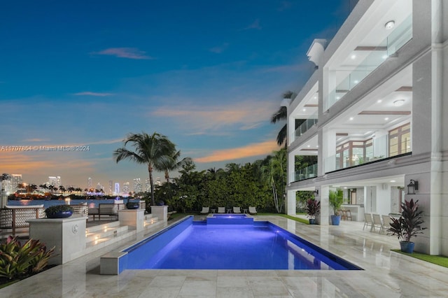 pool at dusk with an in ground hot tub and a patio area