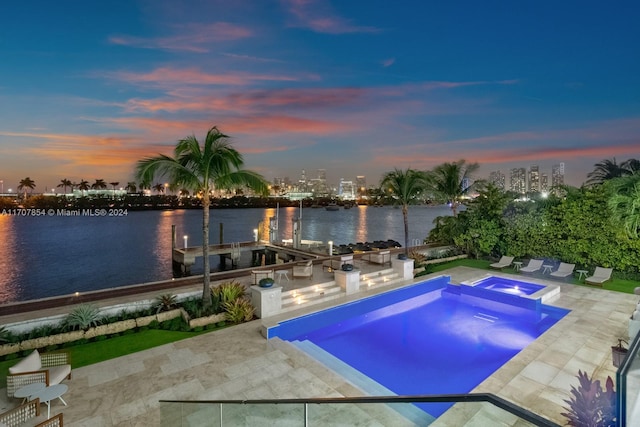 pool at dusk with an in ground hot tub, a water view, and a patio