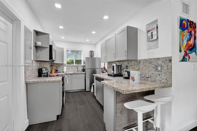 kitchen featuring a kitchen breakfast bar, sink, dark hardwood / wood-style floors, decorative backsplash, and stainless steel appliances