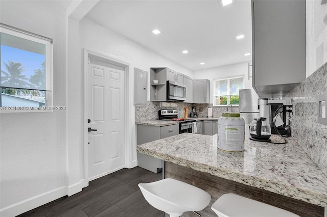 kitchen featuring dark hardwood / wood-style floors, decorative backsplash, appliances with stainless steel finishes, a kitchen bar, and kitchen peninsula