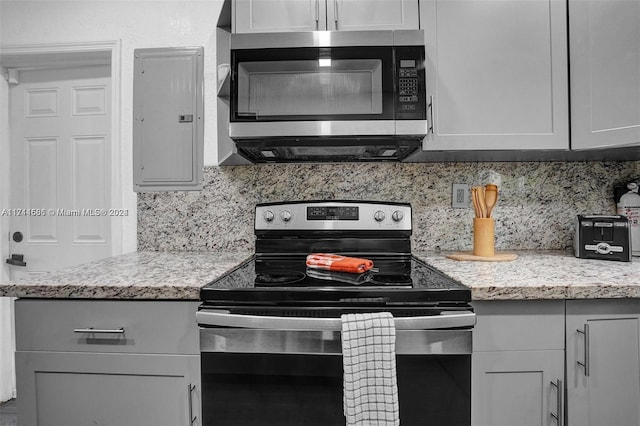 kitchen featuring gray cabinetry, light stone counters, backsplash, electric panel, and appliances with stainless steel finishes