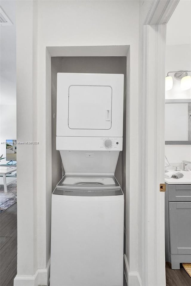 clothes washing area with dark hardwood / wood-style flooring, stacked washing maching and dryer, and sink