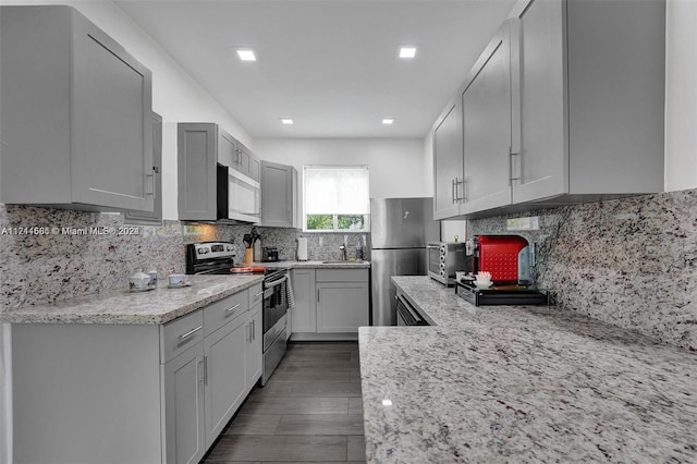 kitchen with decorative backsplash, light stone counters, stainless steel appliances, sink, and dark hardwood / wood-style floors