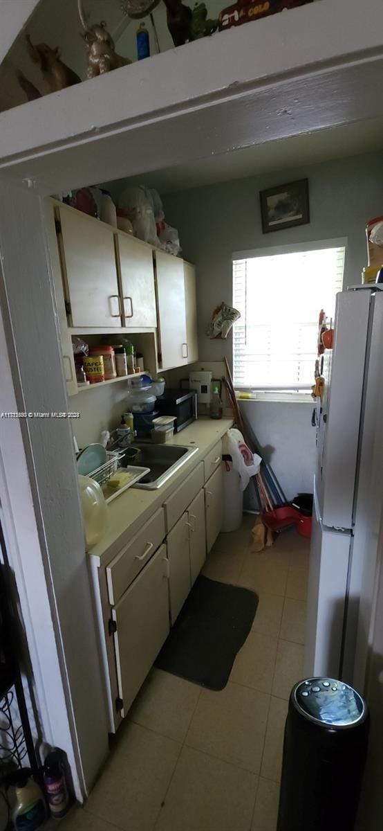 kitchen with white cabinetry, sink, white fridge, and light tile patterned floors