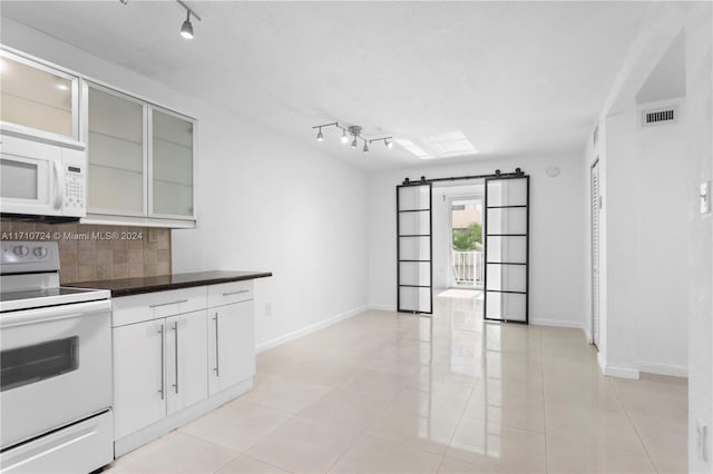 kitchen featuring white appliances, white cabinets, rail lighting, light tile patterned floors, and tasteful backsplash