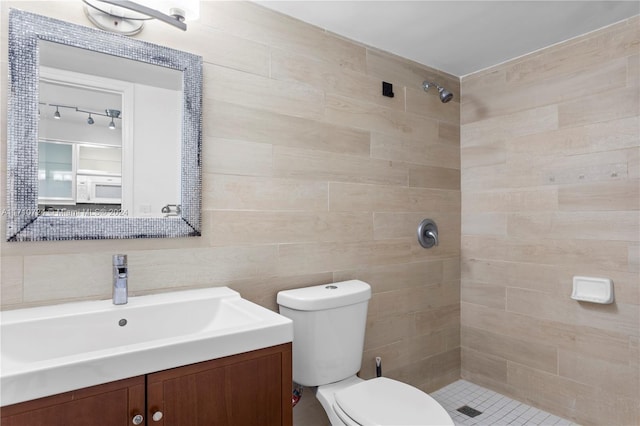 bathroom featuring vanity, toilet, tile walls, and a tile shower