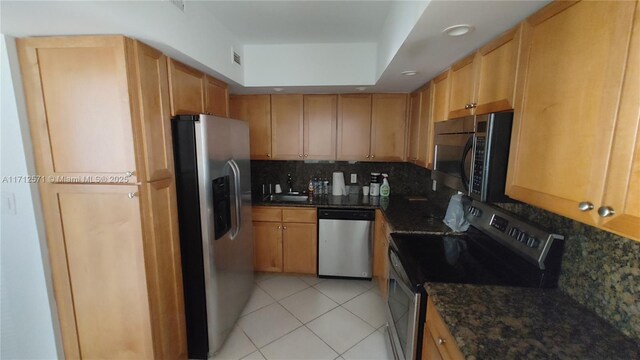 kitchen featuring light tile patterned floors, backsplash, appliances with stainless steel finishes, and dark stone countertops