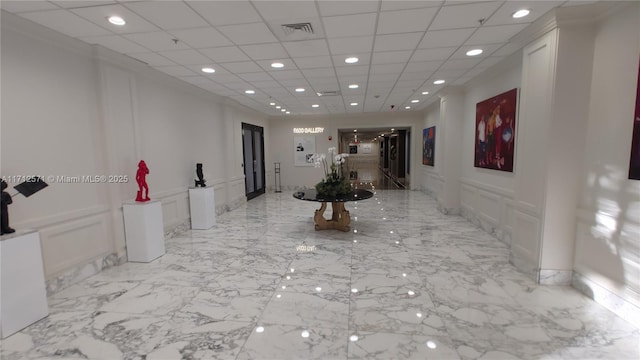 hall featuring wainscoting, a decorative wall, marble finish floor, and visible vents