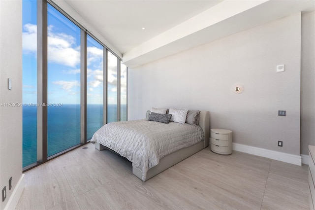 bedroom featuring expansive windows, a water view, light wood-type flooring, and access to exterior