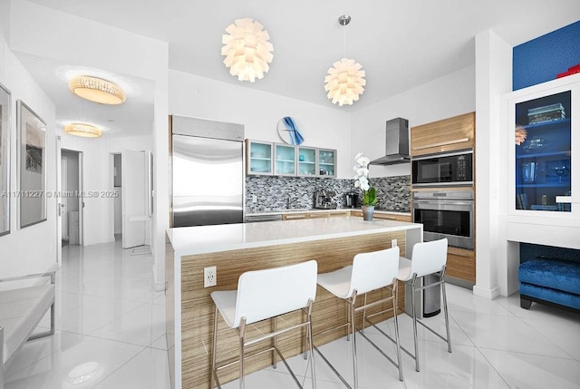 kitchen with wall chimney exhaust hood, built in appliances, pendant lighting, decorative backsplash, and a kitchen island