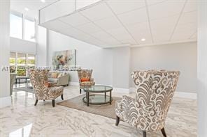 living area featuring a paneled ceiling, marble finish floor, and baseboards