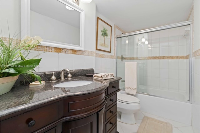 full bathroom featuring bath / shower combo with glass door, vanity, tile walls, tile patterned flooring, and toilet