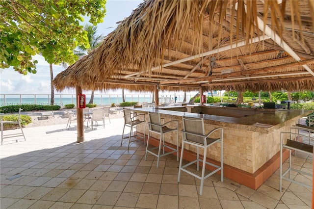 view of patio featuring exterior bar, a gazebo, a water view, and a view of the beach