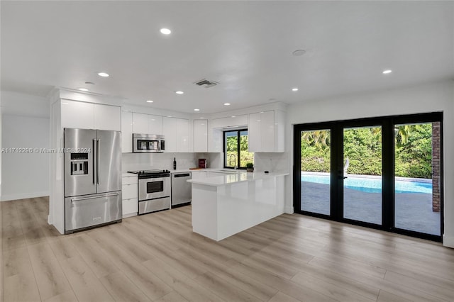 kitchen with kitchen peninsula, appliances with stainless steel finishes, light hardwood / wood-style flooring, and white cabinetry