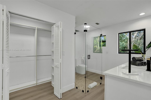 bathroom featuring a shower with door, vanity, wood-type flooring, and toilet