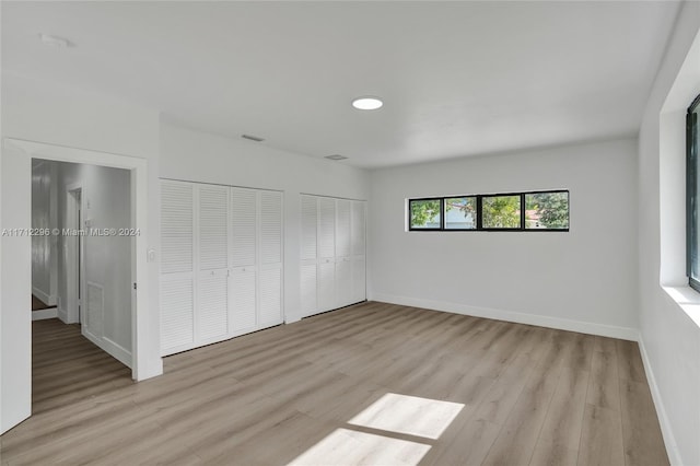 unfurnished bedroom with multiple closets and light hardwood / wood-style flooring