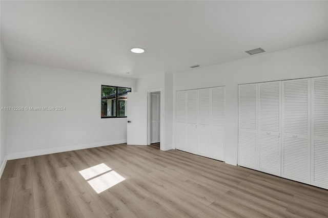 unfurnished bedroom featuring multiple closets and light hardwood / wood-style floors