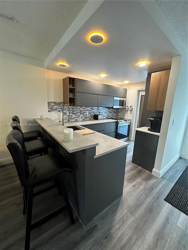 kitchen featuring a textured ceiling, light hardwood / wood-style floors, a kitchen bar, kitchen peninsula, and stainless steel appliances