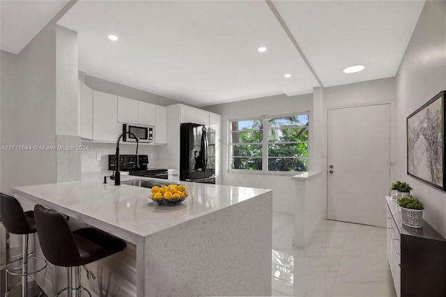 kitchen with kitchen peninsula, a breakfast bar, white cabinets, and black appliances