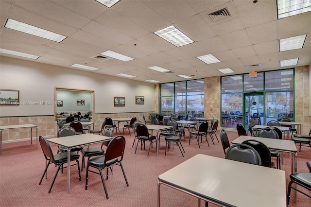 dining area with carpet, a drop ceiling, and a wall of windows