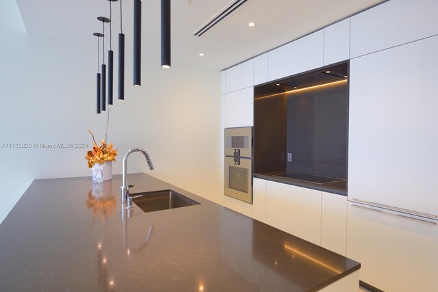 kitchen with floor to ceiling windows, white cabinetry, sink, and pendant lighting