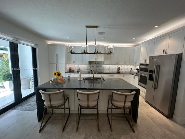 kitchen with white cabinetry, appliances with stainless steel finishes, a center island with sink, and decorative light fixtures