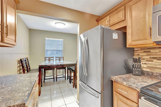 kitchen with stainless steel fridge, tasteful backsplash, light brown cabinets, dark stone countertops, and light tile patterned flooring