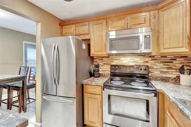 kitchen featuring decorative backsplash, light stone counters, light tile patterned floors, and stainless steel appliances