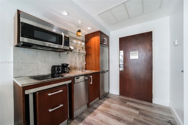 kitchen with appliances with stainless steel finishes, light wood-type flooring, backsplash, light stone counters, and sink