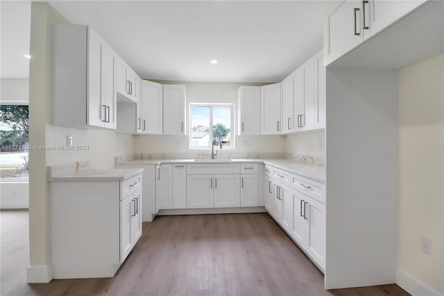 kitchen with light stone countertops, light wood-type flooring, white cabinetry, and sink