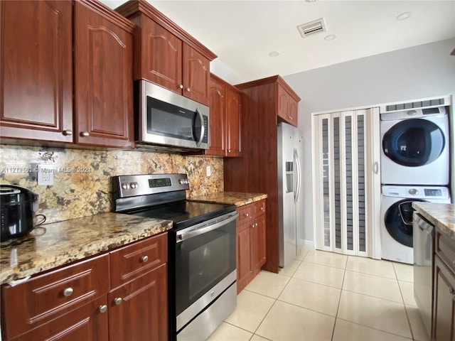 kitchen featuring light stone countertops, backsplash, stacked washer / dryer, light tile patterned floors, and appliances with stainless steel finishes