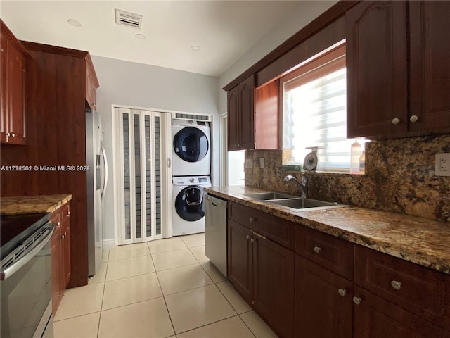 kitchen featuring sink, stacked washing maching and dryer, decorative backsplash, light tile patterned floors, and appliances with stainless steel finishes