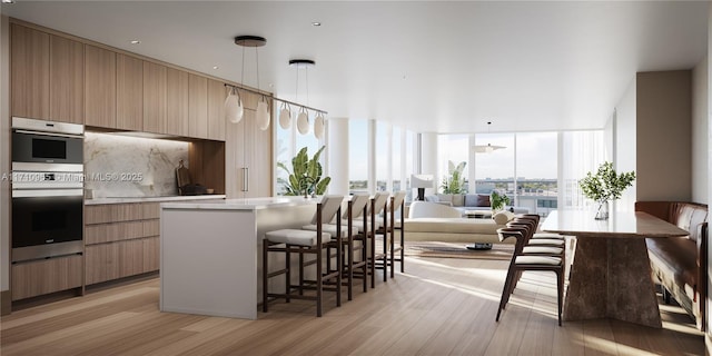 kitchen with decorative light fixtures, stainless steel double oven, light wood-type flooring, and a breakfast bar area