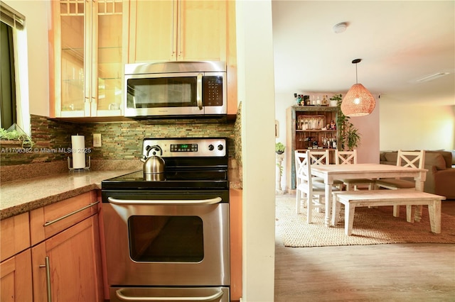 kitchen with wood-type flooring, backsplash, stainless steel appliances, and hanging light fixtures